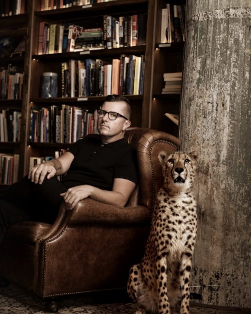 Steve Cunningham in his library, seated in a leather armchair, with a cheetah beside him